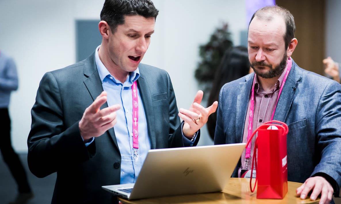 two men talking in fronot of laptop